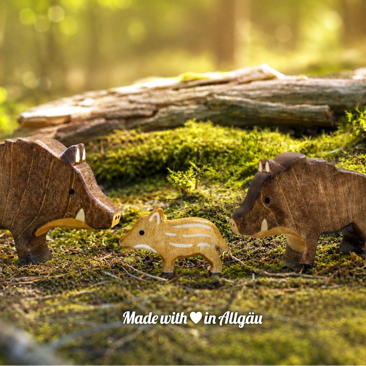 Handgefertigtes Holzspielzeug Wildschwein-Familie von Allgäuer Holztiere mit Keiler, Bache und Frischling, auf einem moosbedeckten Waldboden vor einem Baumstamm arrangiert, umgeben von natürlichen Waldmaterialien, im Hintergrund eine unscharfe Waldlandschaft, aus bayerischem Ahornholz gefertigt, mit pflanzlichen Farben in Braun-, Hellbraun- und Schwarztönen bemalt, im Allgäu produziert und für Kinder ab 3 Jahren geeignet.