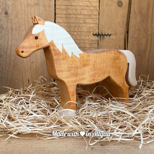 Handgefertigtes Holzspielzeug Pferd Haflinger Stute von Allgäuer Holztiere, stehend auf Holzspänen im Hintergrund raues Holz, aus bayerischem Ahornholz gefertigt, mit pflanzlichen Farben rot-braun bemalt, im Allgäu produziert und für Kinder ab 3 Jahren geeignet.